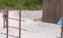a woman in a pink bikini is standing in front of a fence on a beach .