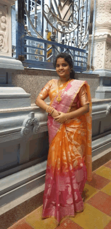 a woman in a pink and orange saree stands next to a wall