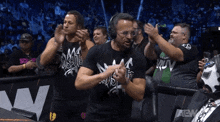 a group of men wearing black shirts that say aew are clapping their hands