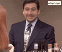 a man in a suit and tie is smiling while standing in front of a bottle of wine .