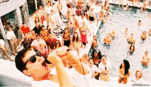 a group of people are gathered around a swimming pool and a man is drinking from a cup