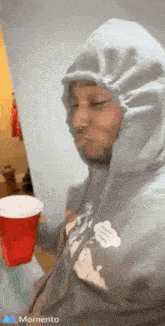 a man in a hoodie is holding a red cup and making a face .