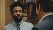 a man in a blue shirt and tie looks at another man