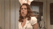 a woman wearing bunny ears is standing in front of a skeleton in a room .