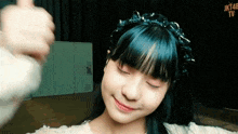 a girl with blue hair is wearing a headband and giving a thumbs up
