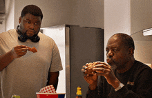 a man wearing headphones is eating a chicken nugget while another man is eating a hamburger