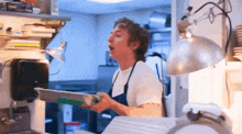 a man in an apron is holding a tray in a kitchen