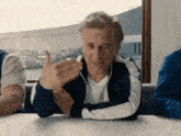 a man is sitting at a table with his hands outstretched and talking to another man .