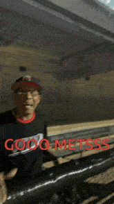 a man wearing a hat and glasses is standing next to a chain link fence with the words good metsss written on it