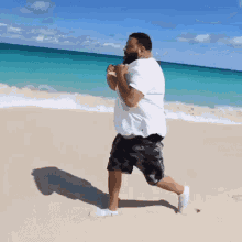 a man in a white shirt and black shorts is running on a beach .
