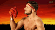 a shirtless man is holding a bloody heart in front of a sunset with the word fite on the bottom