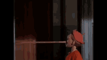 a wooden puppet with a long nose and a red hat is standing in a doorway .
