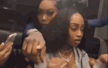 two women are sitting next to each other on a plane and one of them is smoking a cigarette .