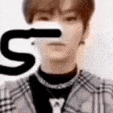 a close up of a man wearing a plaid jacket and a necklace with the letter s on his face .