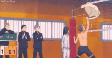 a group of people are standing around a volleyball net watching a man without a shirt jump over it .