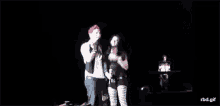 a man and a woman are standing next to each other on a stage in the dark .