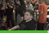 a man with green hair is sitting in a chair in front of a group of people