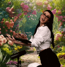 a woman wearing glasses and a white shirt is kneeling in front of a microphone with flowers in the background