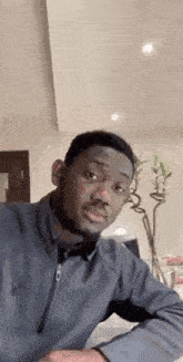 a man in a gray jacket is making a funny face while sitting at a table in a living room .