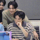 a group of young men are sitting in a room . one of the men is wearing a striped sweater .
