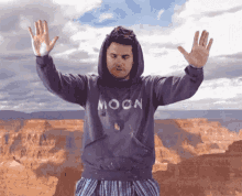 a man wearing a hoodie that says moon holds his hands up in the air