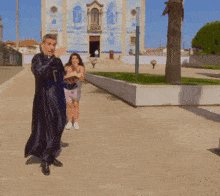 a man in a black robe is holding a cross in front of a blue and white building