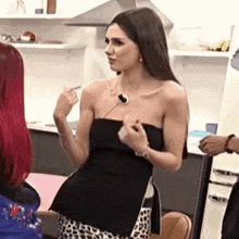 a woman in a black strapless top and leopard print skirt is standing in a kitchen talking to another woman .
