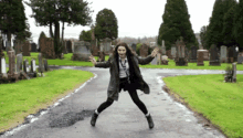 a woman is jumping in the air in a cemetery with her arms outstretched