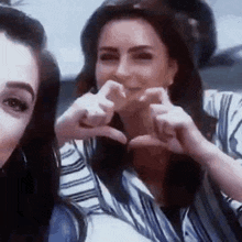 two women are making a heart shape with their fingers .