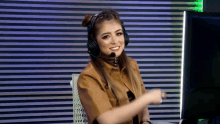 a woman wearing headphones and a microphone smiles while sitting in front of a computer monitor