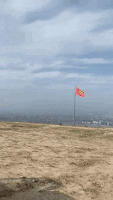 a red flag is flying in the wind on top of a dirt field .
