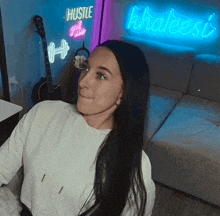 a woman sits in front of a neon sign that says hustle