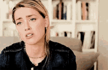 a woman in a denim jacket is sitting on a couch in front of a bookshelf and making a funny face .