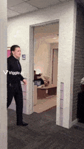 a woman in a suit and tie walks through a doorway with a viggle.ai sticker on the wall