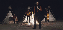 a man in a red shirt is standing in front of a fire while playing instruments
