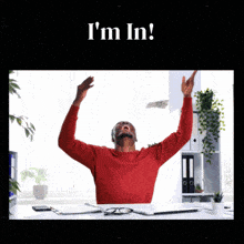 a man in a red sweater is sitting at a desk with his arms in the air and the words i 'm in