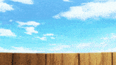 a wooden fence in front of a blue sky with white clouds