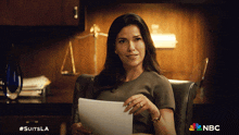 a woman sitting in a chair holding a piece of paper with nbc written on the bottom