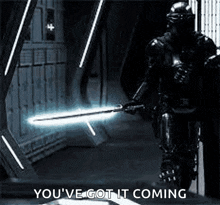 a man in armor is holding a light saber in a dark room and saying `` you 've got it coming '' .