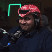a man wearing headphones and a head scarf smiles while standing in front of a microphone