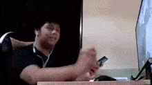 a man is sitting at a table playing a video game while wearing headphones and holding a remote control .