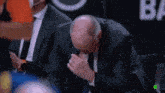 a man in a suit is sitting in front of a sign that says ' b ' on it