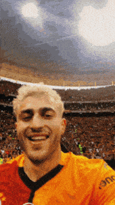a man wearing an orange shirt with the word eme on it smiles in front of a crowd