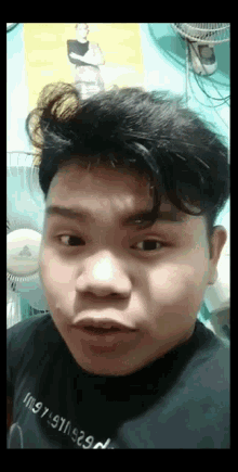 a young man is making a funny face in front of a wall fan