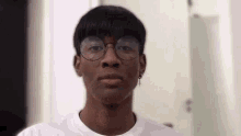 a young man wearing glasses and earrings is making a funny face .