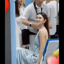 a woman in a blue dress is sitting in a chair and smiling while a man adjusts her hair .