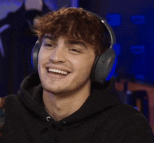 a man wearing headphones and a black hoodie is smiling