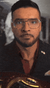 a man wearing glasses and a suit is holding a boxing belt