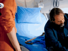 a man in a hospital bed with a blue blanket and a cane