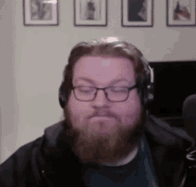 a man with a beard wearing headphones and glasses is sitting in front of a microphone .